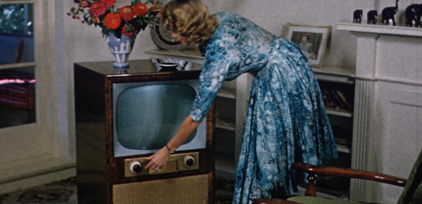 1950s image of a woman turning on a television set in her living room.