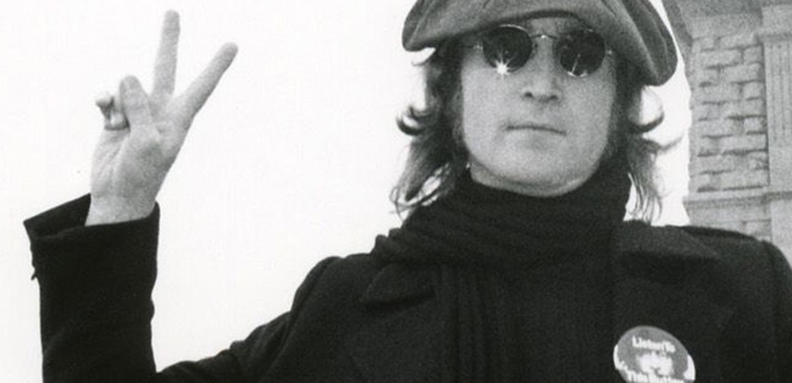 Head and shoulders shot of John Lennon pictured in New York, wearing sunglasses and a beret and making a peace sign with his fingers. C. 1973.