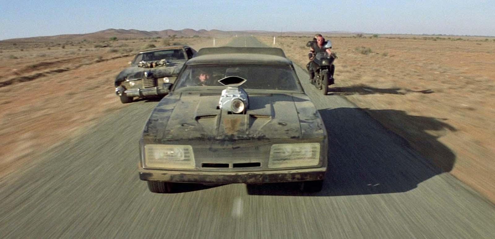A souped-up car speeding down a desert highway in Mad Max 2, flanked by another car and a motorbike