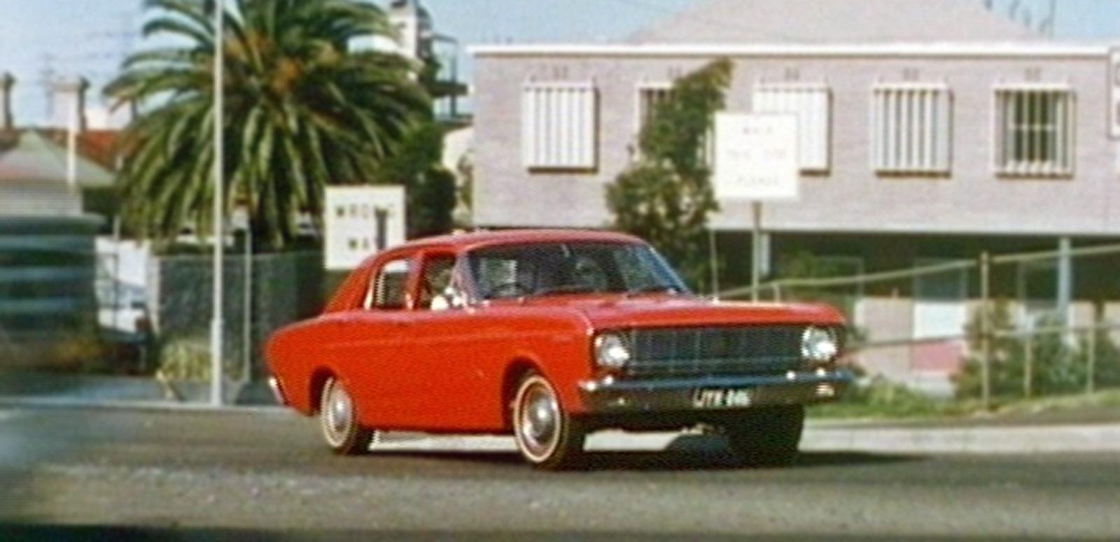 A red 1968 Ford XT Falcon drives along a suburban street.