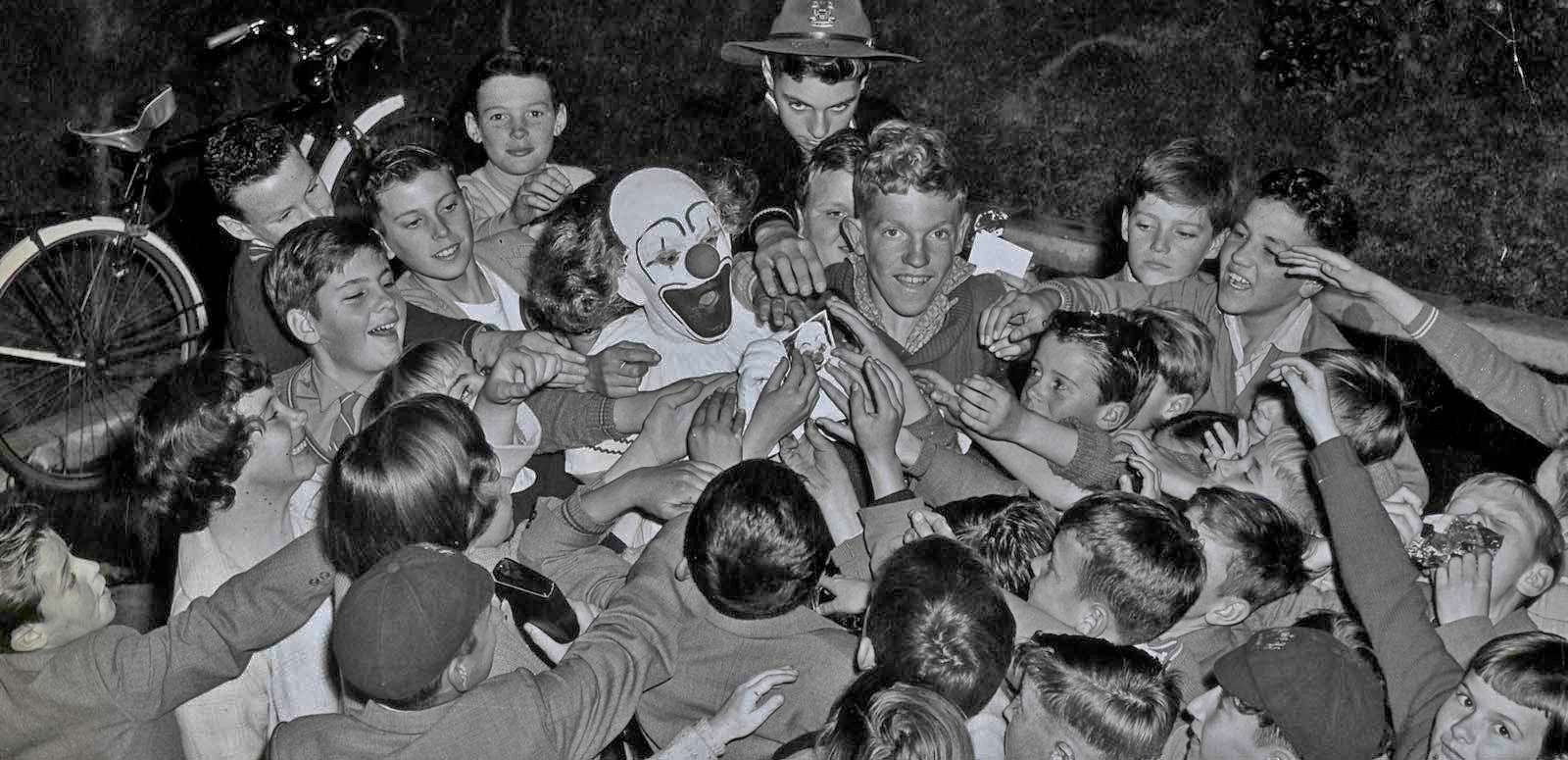 Bobo the clown is surrounded by a crowd of children reaching out to touch him