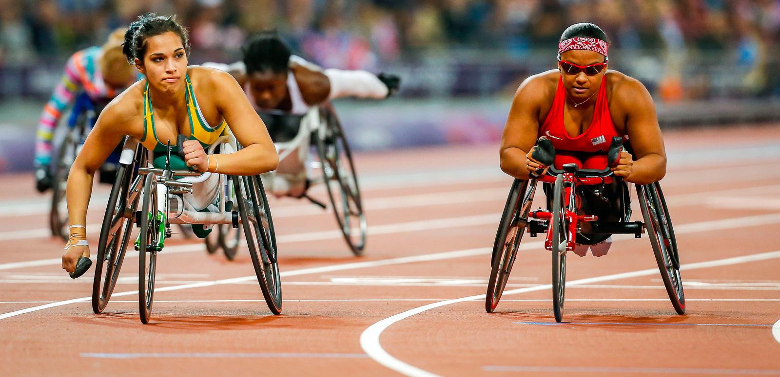 Women wheelchair athletes competing on an Olympic race track. There are two in the foreground who are side by side and another two can be seen further down the track.