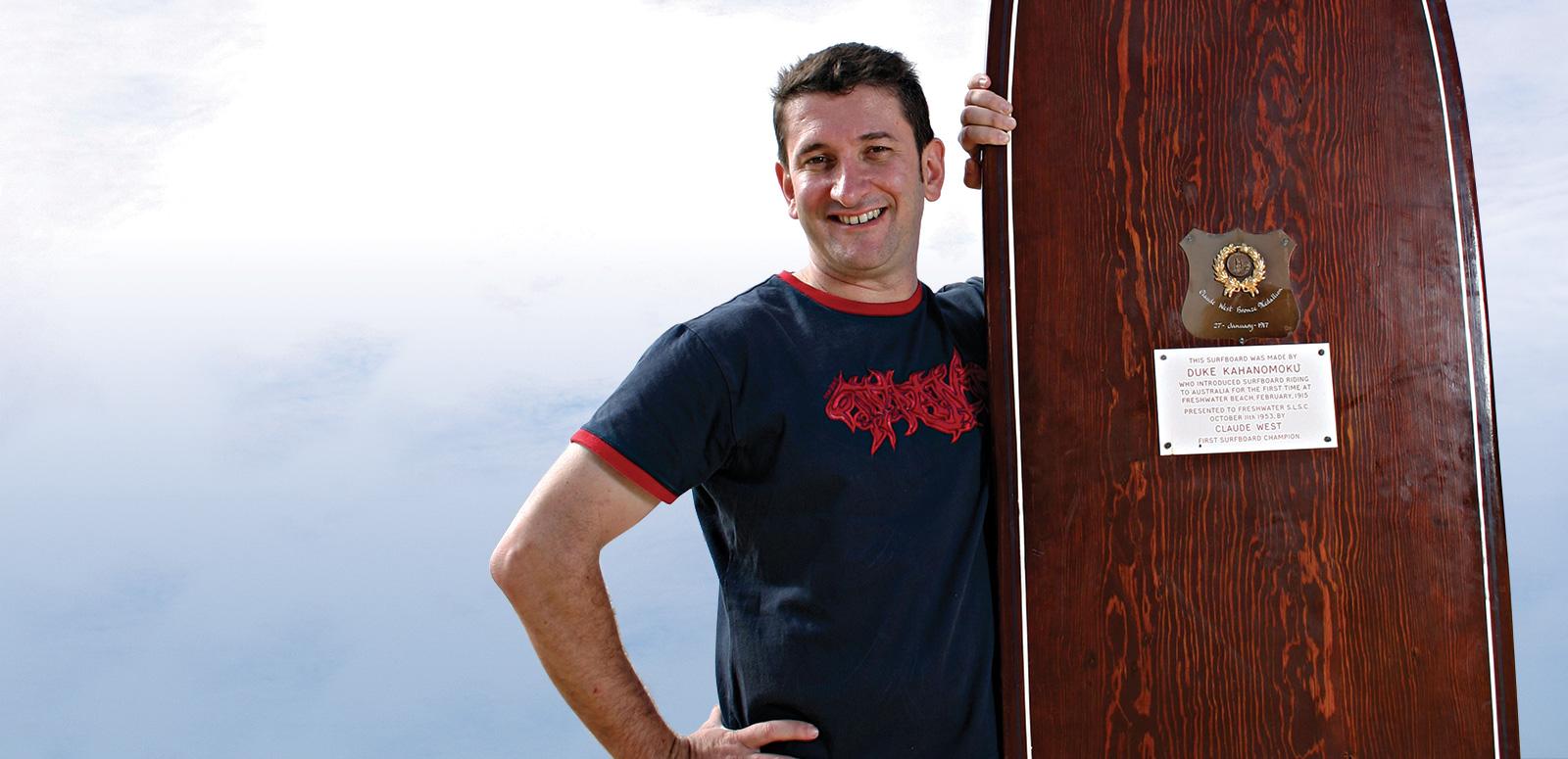 Warren Brown standing next to a large wooden surfboard