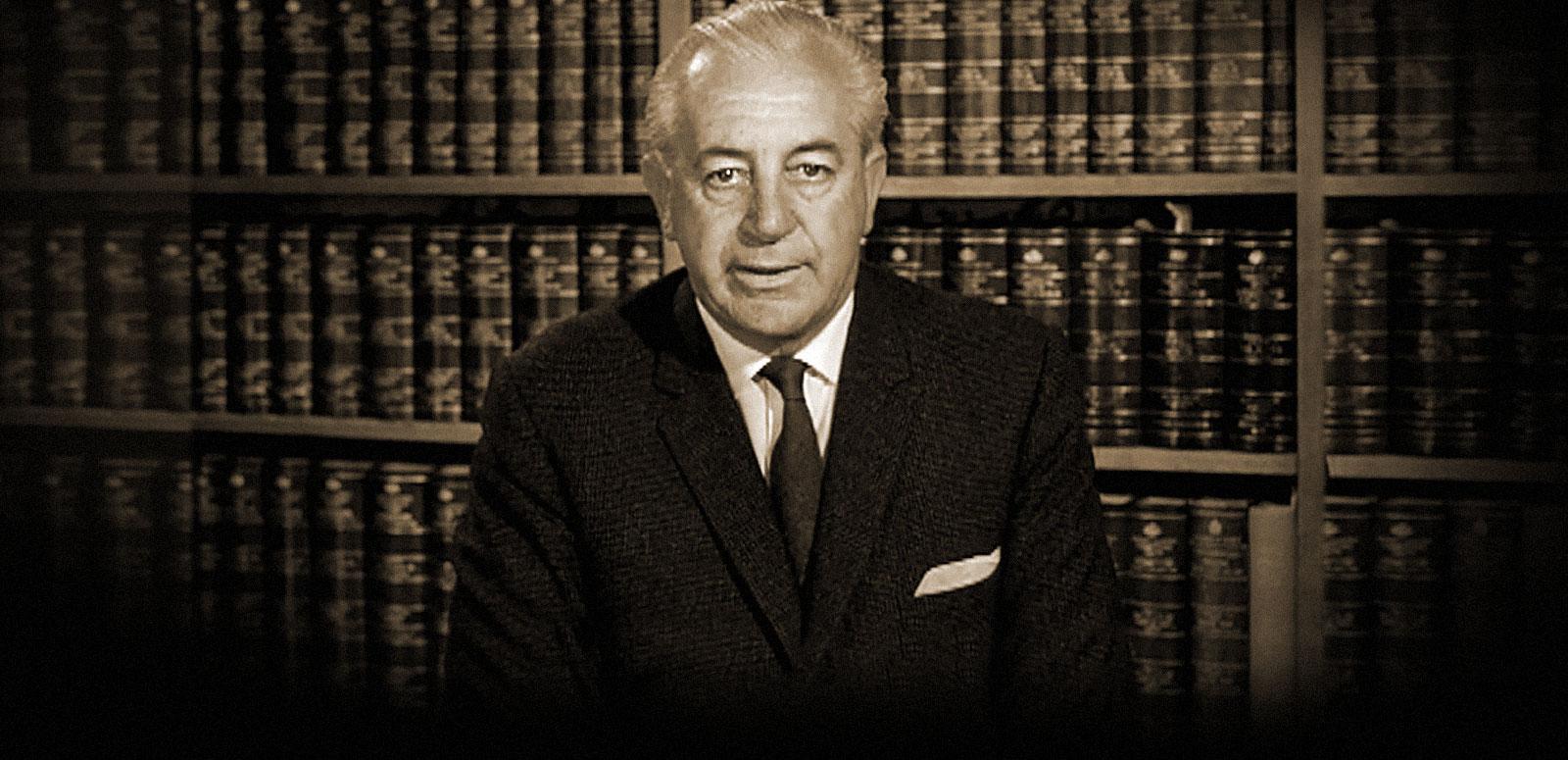 A sepia image of Harold Holt as federal treasurer, seated behind a desk and recording an address to the nation