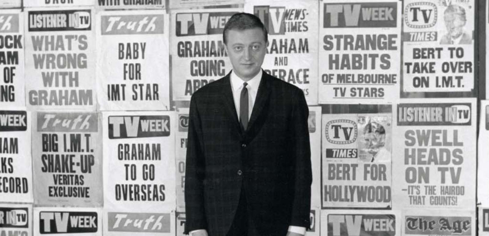 Graham Kennedy standing in front of a wall full of newspaper headlines about himself.