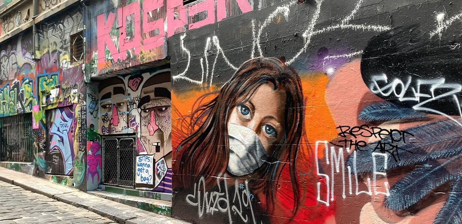 A graffitti painted on a wall, showing a youg woman wearing a face mask and the word SMILE, taken from the Australia Locked Down project.