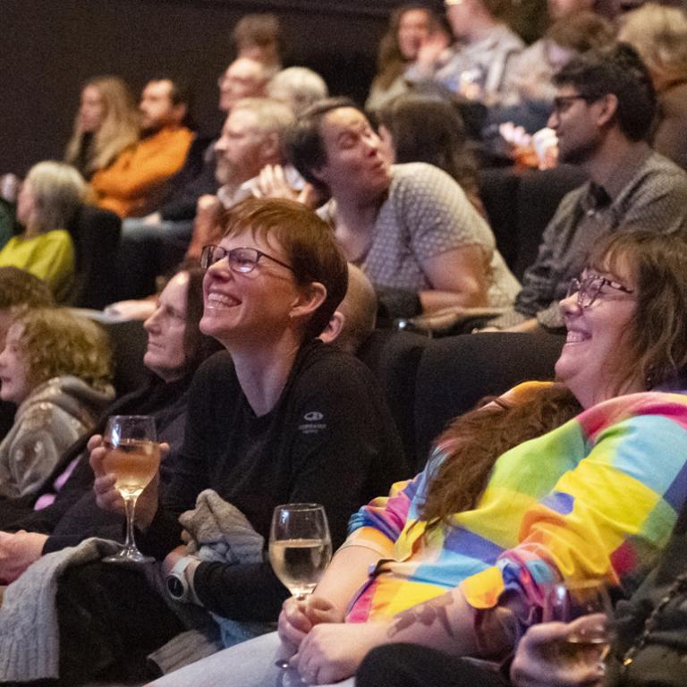 Crowd sitting in a theatre drinking champagne and laughing