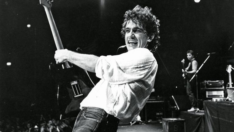 Guitarist Ian Moss from the band Cold Chisel on stage during a concert, smiling and leaning backward as he holds his guitar upright. 