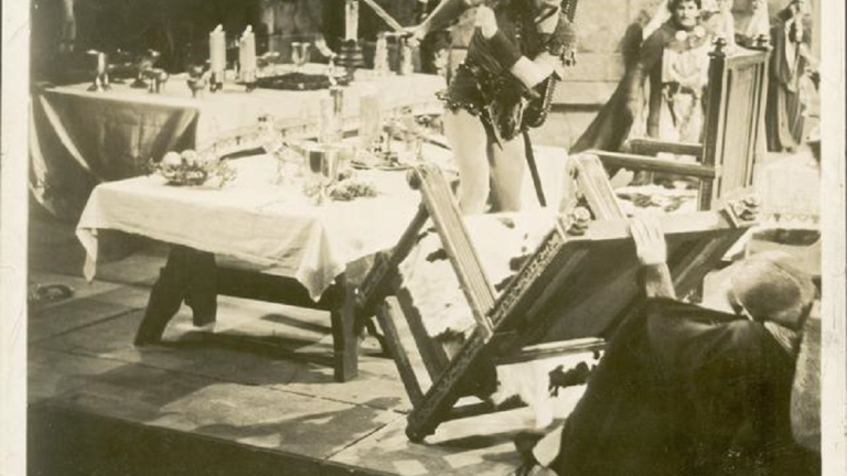 Errol Flynn upturns a table in a baqueting hall.