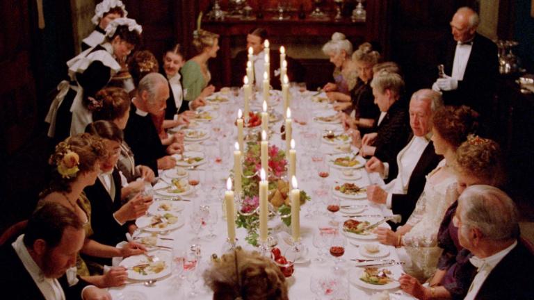 A large 1890s dinner party is in full swing as seated guests converse and eat while being served by maids and a butler in a scene from My Brilliant Career