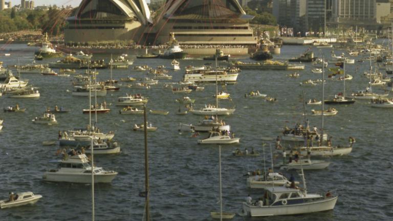 The Sydney Opera House and Sydney skyline as seen on the day of the Sydney Opera House's opening. Pleasure craft dot the harbour.