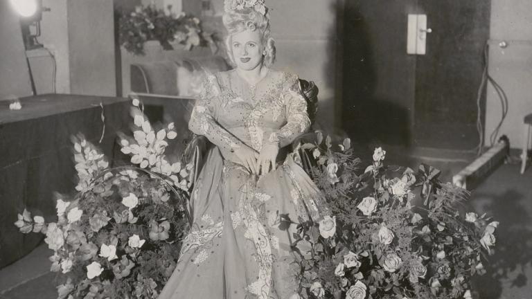 Marjorie Lawrence wearing an exotic dress and surrounded by flowers.