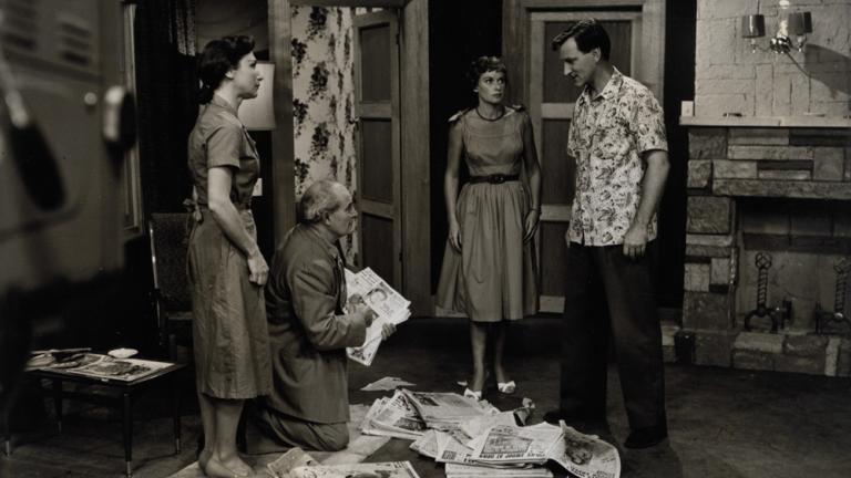Three people in a studio set feature in this black and white production still.