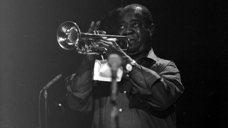 Jazz musician Louis Armstrong playing a trumpet in front of a microphone, circa 1964.