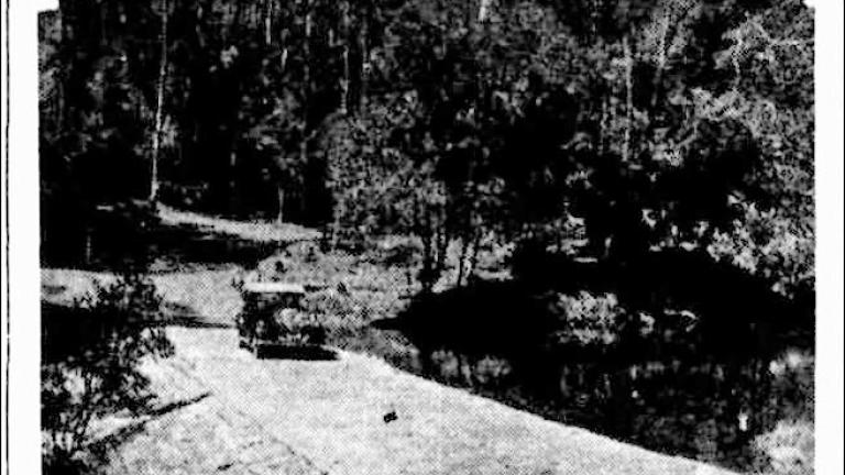 Newspaper image showing a 1930s motorcar driving across the Upper Causeway by the water in Sydney's Royal National Park
