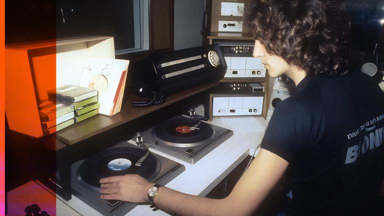 Radio and TV personality Lee Simon sitting in a radio studio in front of some turntables. He is turned slightly away from the camera.