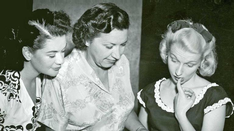 1940s radio producer Grace Gibson holding the script for a radio drama, flanked by two younger female actors looking at the script she is holding