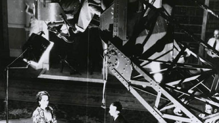 Overhead production shot of Merle Oberon acting with a movie camera on a crane above her