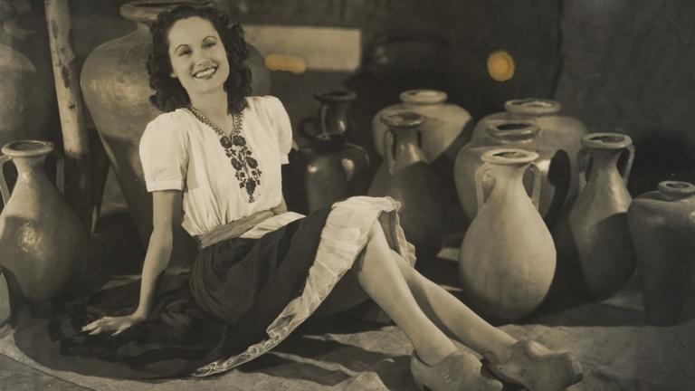 Betty Bryant on the set of Forty Thousand Horsemen wearing a peasant dress and reclining among earthenware pots.