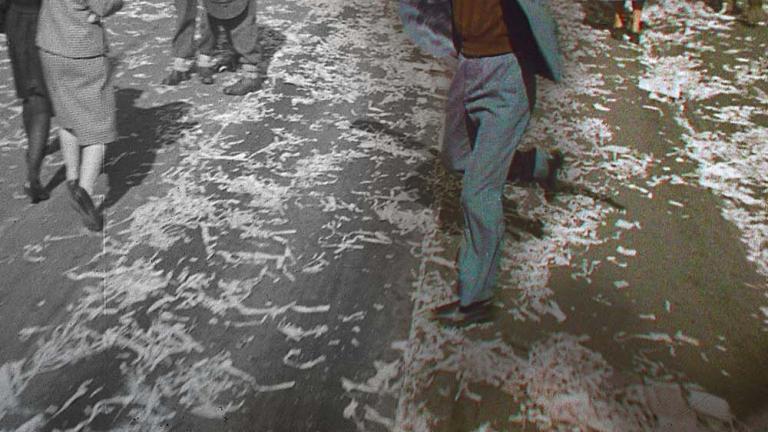 A partly colourised image of a man dancing with raised hat in Sydney, part of a crowd celebrating the end of the Second World War