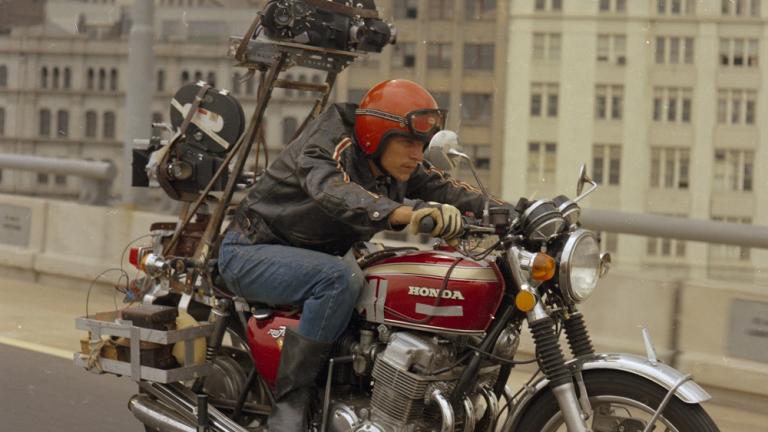 A man rides a motorcycle with a camera mounted on the back.