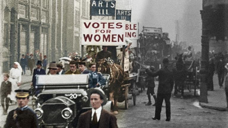 Colourised film still of a procession of university students marching for women's right to vote in Sydney. Sign reads: Votes for Women.