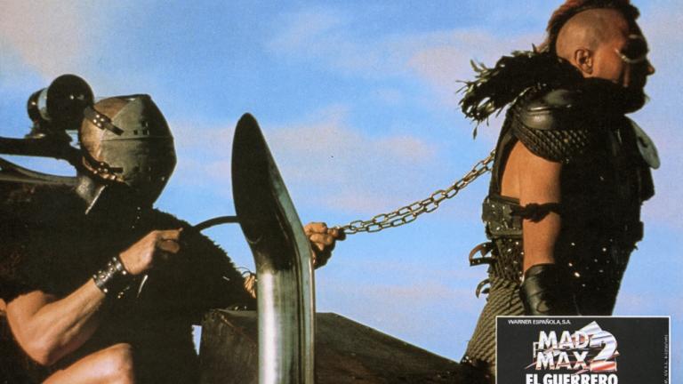 Mad Max 2 lobby card showing Wez (Vernon Wells) chained by the neck by Humungus (Njell Nilsson). 