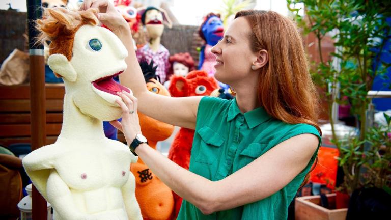 A women examines a lifesize puppet in an open air market.