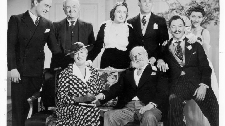 The cast from the film Dad and Dave come to town, seated on and standing around a sofa, smiling at camera.