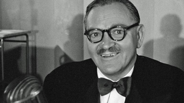 Head and shoulders shot of a man in a suit and bow tie, wearing glasses and smiling at camera.