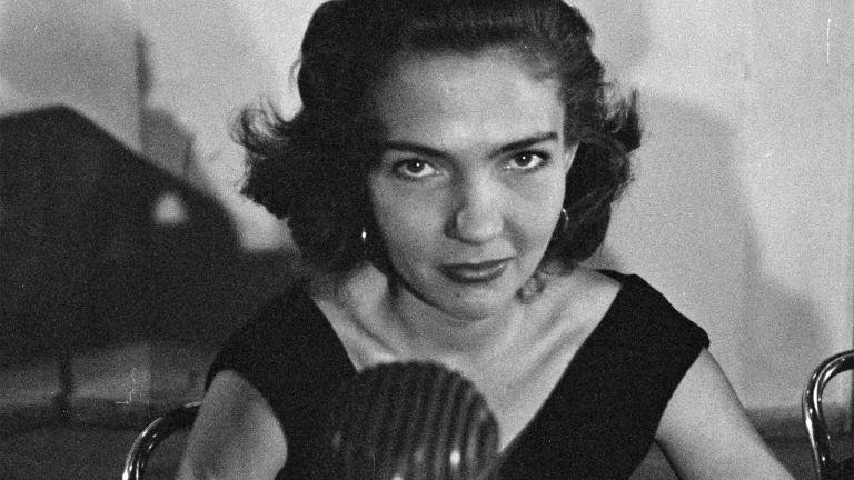 Head and shoulders shot of a young woman looking at camera with a radio mic in front of her.
