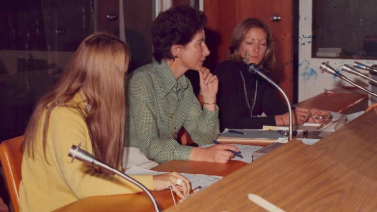 Three women in a television control room. The woman in the centre appears to be calling the shots and has her hand in a thinker's pose on her chin.
