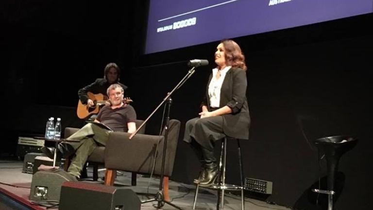 Christine Anu on stage at the NFSA. In the background, Curator Thorsten Kaeding, and a musician holding a guitar