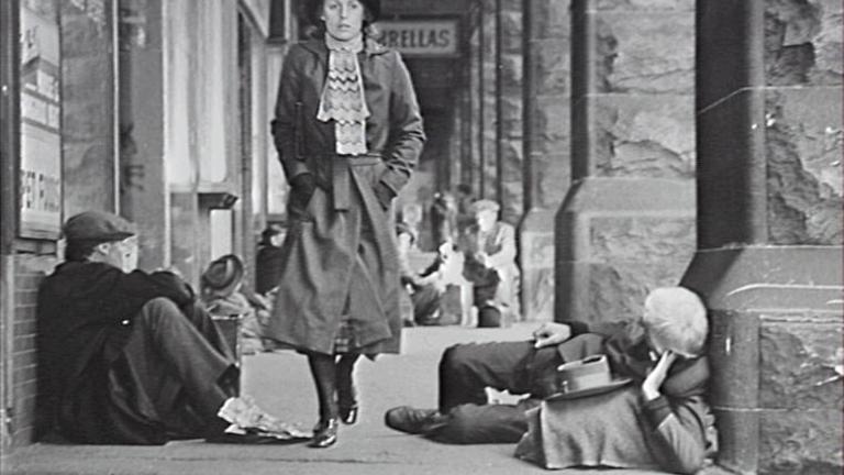 Film still of Caddie walking past homeless men at Central Station, Sydney durng the Depression.