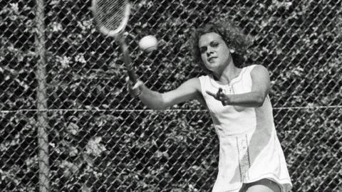 Evonne Goolagong-Cawley holding a wooden tennis racket and about to hit a tennis ball.