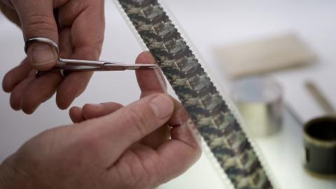 A photographic strip is being cut by a technician