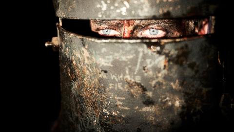 Close up a man's eyes peering out of a Ned Kelly helmet