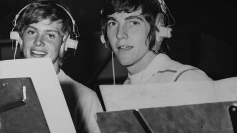 John Farnham and Jeff Phillips wearing headphones and standing behind music stands during a session in the recording studio in 1970