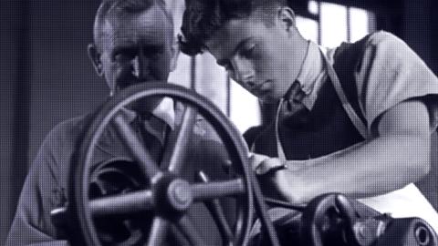 A teenage boy and a teacher standing over a wheel in a workshop.