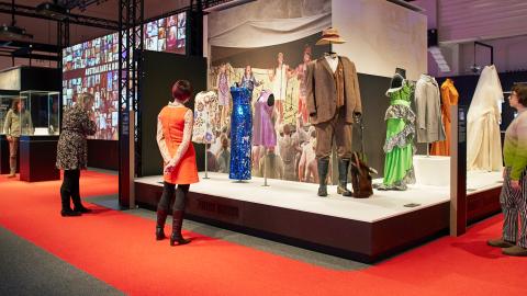 Some people in an exhibition space looking at different movie costumes on mannequins. 