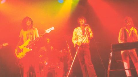 The 5 male members of 1970s rock band Sherbet performing on stage: a lead guitarist, bass guitarist, drummer and keyboards player with lead singer Daryl Braithwaite