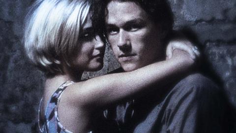 Heath Ledger as Jimmy and Rose Byrne as Alex in a still from Two Hands. The shot is grainy and plays with focus. They are in an embrace while they lean on a wall. Ledger looks at the camera.