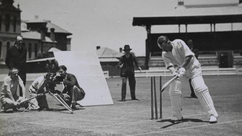 Donald Bradman batting in front of wickets while a film crew films him from behind