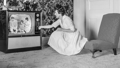 A woman kneeling down to adjust a television, c1950s.