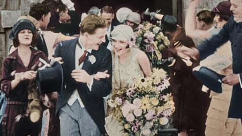The celebrating bride and groom and wedding party exit the church after a wedding in 1925