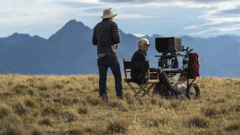Cinematographer Ari Wegner standing next to director Jane Campion, seated at a monitor, on a grassy mountain location in New Zealand for the movie The Power of the Dog