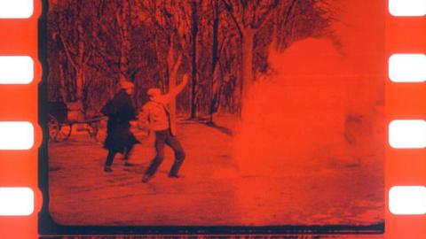 Frame of early silent film that has been tinted red showing two men in a forest pointing to the sky