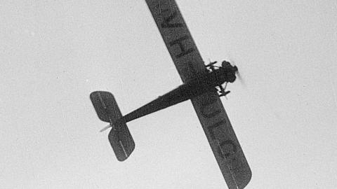 An early 20th century aeroplane flies overhead, seen from below with the letters VH-ULG visible on the underside of the wings