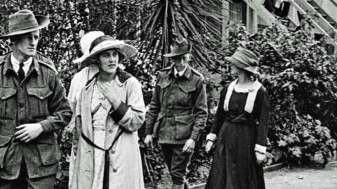 Two Australian soldiers from the First World War walk in uniform, accompanied by three women