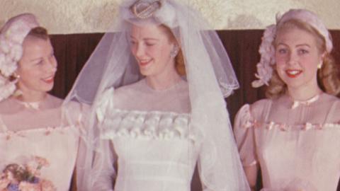 Three women pose for the camera. One wears a white wedding gown. The other two are bridesmaids in pink.